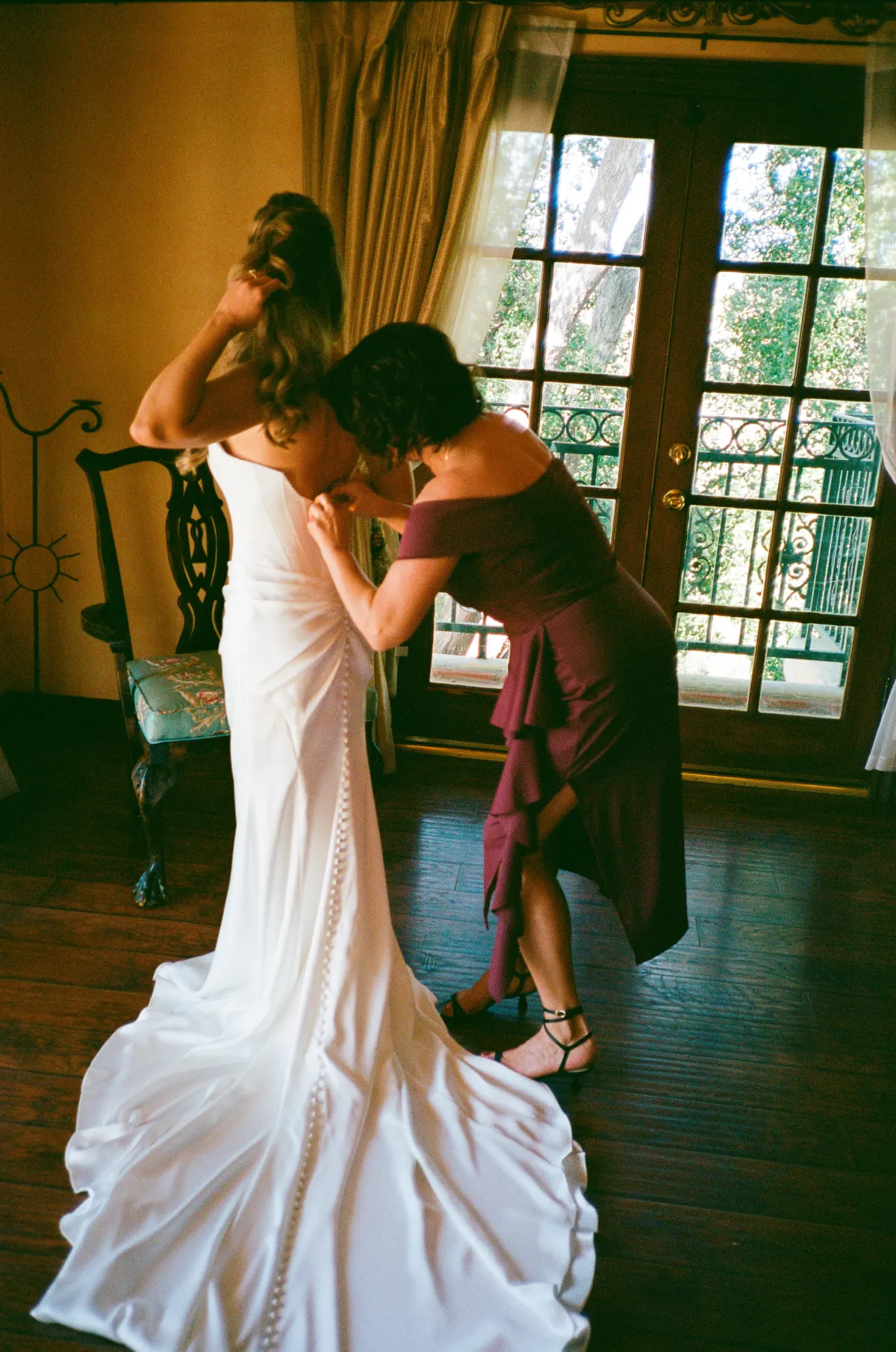 Mother helping bride into her wedding dress, soft window light