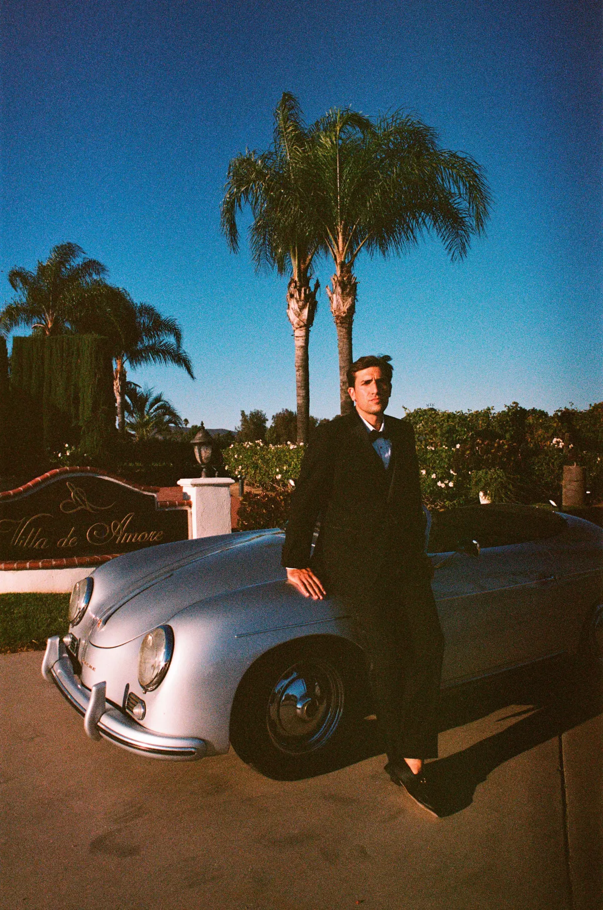 Groom leaning on retro convertible at dusk