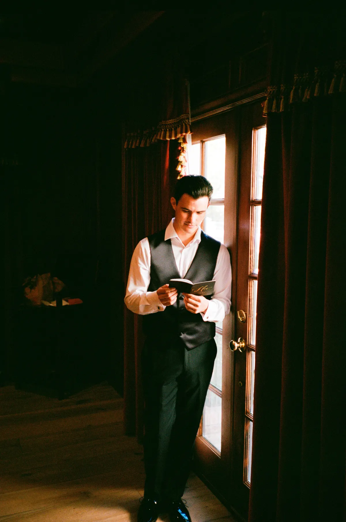 Groom reading vows by window in dark room