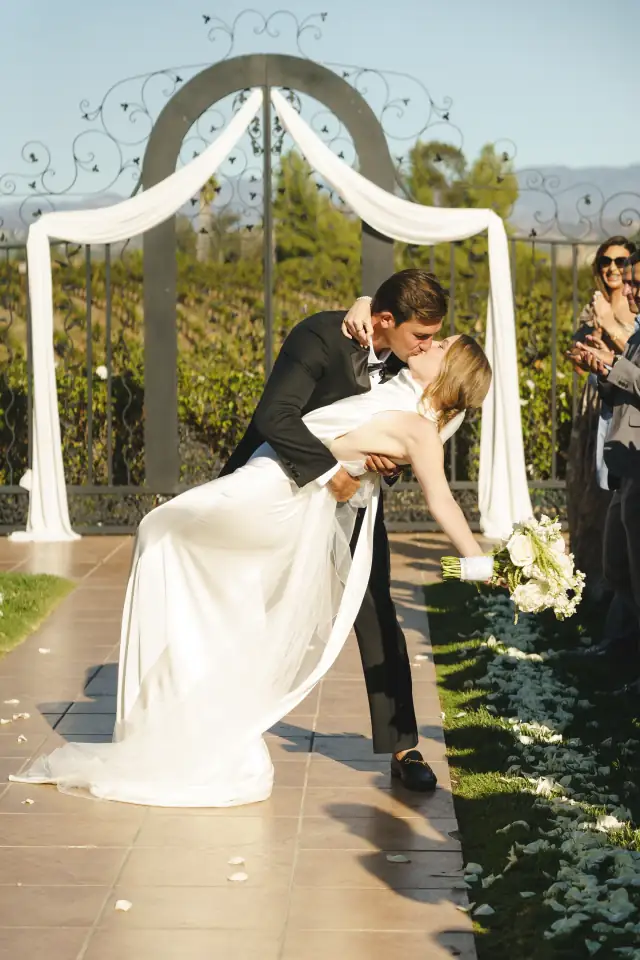Newlyweds kissing beneath the white ceremony arch at Villa de Amore