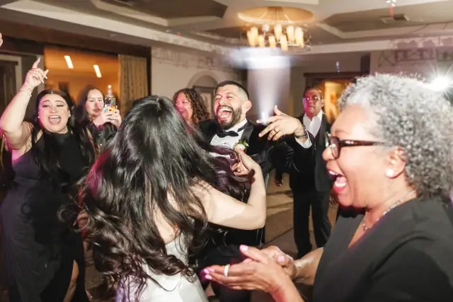 Guests joyfully dancing and celebrating at an indoor wedding reception with a bride and groom.