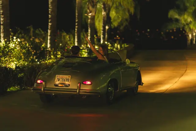 Newlyweds driving away from Villa de Amore in a classic car at night