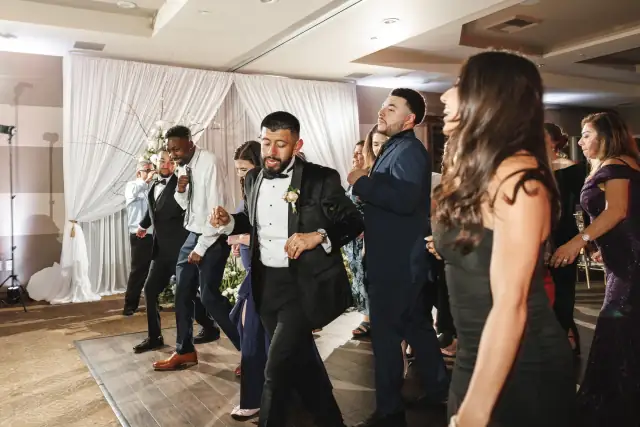 Guests dancing together at Grace and Oscar's indoor wedding reception with white drapery and floral decorations in the background.