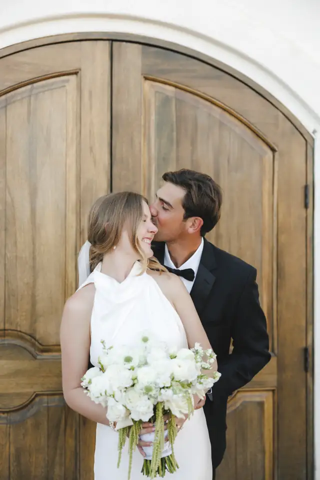 Newlyweds kissing in front of Villa de Amore's wooden doors
