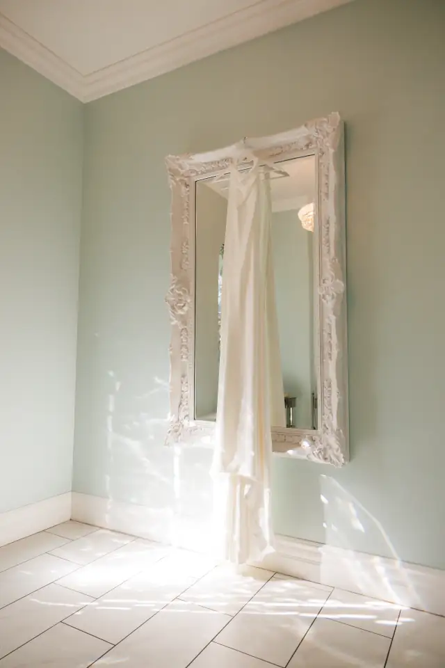 Wedding dress hanging beside an ornate mirror at Villa de Amore